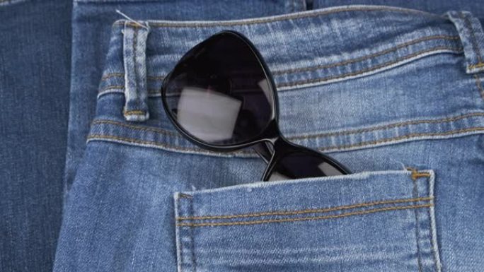 太阳镜从女式牛仔裤的后口袋里伸出来。全景。