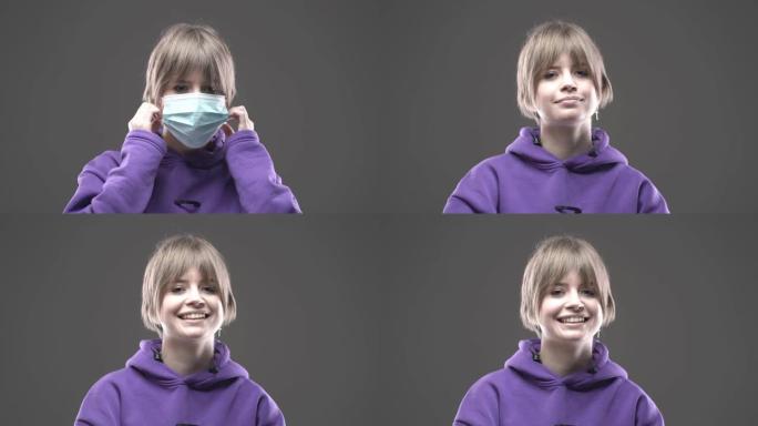 灰色工作室墙上戴着医用口罩的女孩脱下防护口罩，微笑。检疫结束，科罗娜病毒被击败