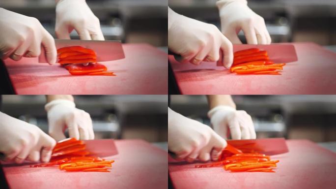 烹饪。厨师，戴着防护手套，切成红色的甜椒，将胡椒切成薄片。特写视图