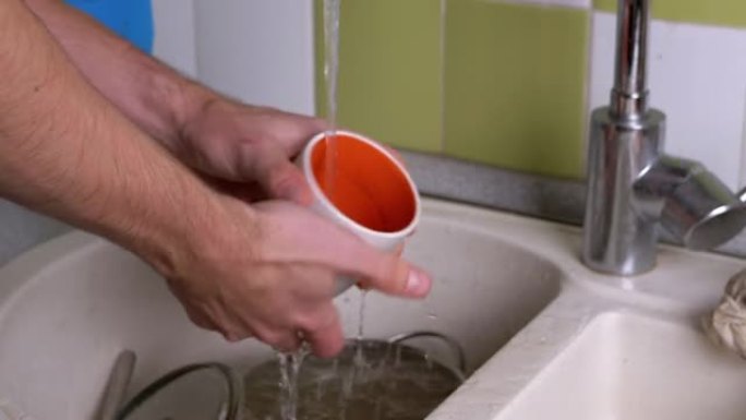 男性手在流水下洗脏杯子，厨房水槽里的勺子