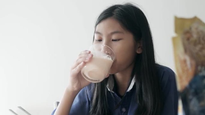 快乐的亚洲女孩穿着运动服，早上上学前喝一杯牛奶，生活方式理念。