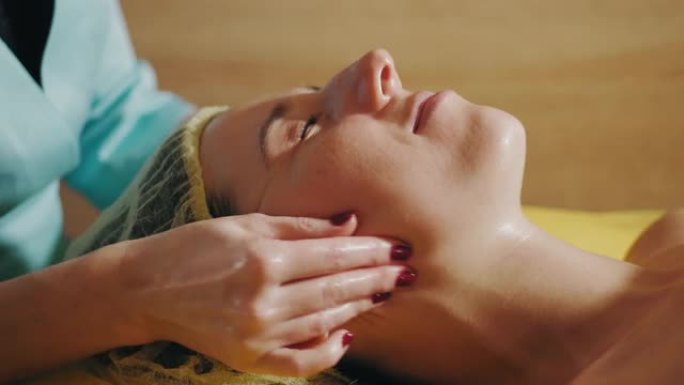 抗衰老程序，面部按摩。特写。女人躺在沙发上，在美容诊所接受面部按摩，以调理肌肉和面部皮肤淋巴引流。护