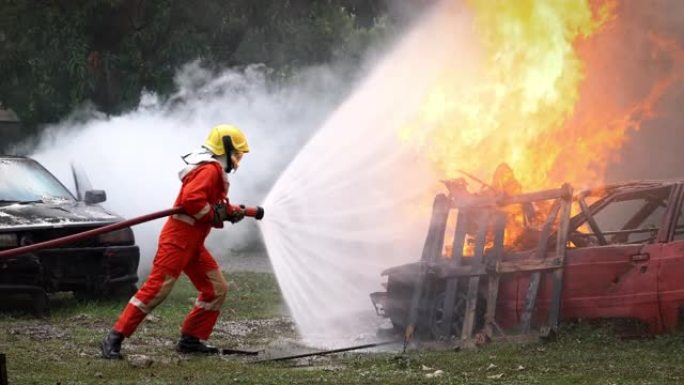 勇敢的消防员穿着消防服，负责安全救援工作，从消防水带喷洒水，扑灭爆炸燃烧汽车上的crack啪作响的火