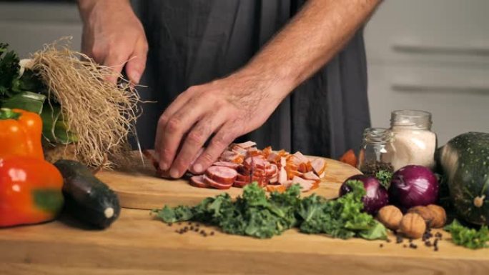 这个人正在切蔬菜之间的木板上的香肠。自制香肠。在厨房的所有风景中，相机慢慢移到显示桌子空间的一侧。