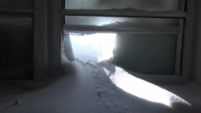 在荒芜的城市废弃房屋的破碎冰冻窗户上下雪。