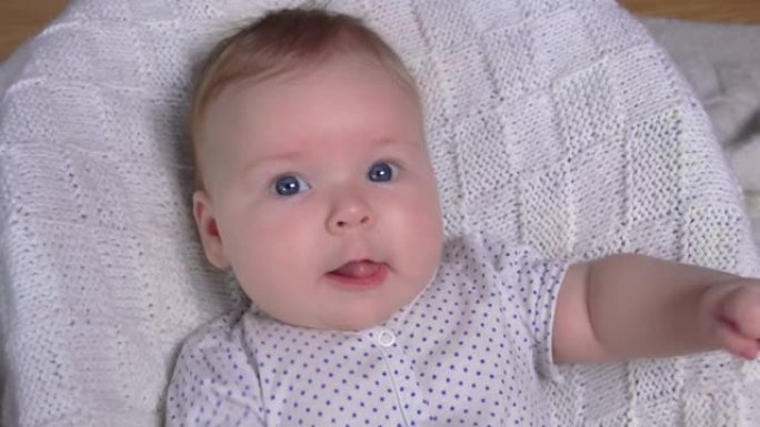 一个可爱的开朗婴儿躺在针织毯子上挥舞着双手