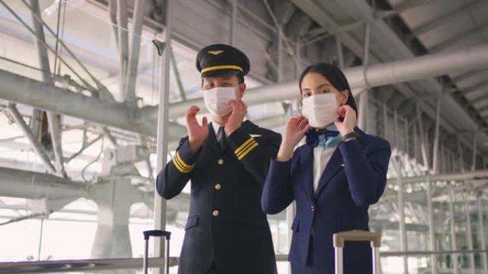 在COVID大流行期间，戴着口罩的客机飞行员和空姐在机场航站楼走到飞机上，以防止冠状病毒感染。航空运