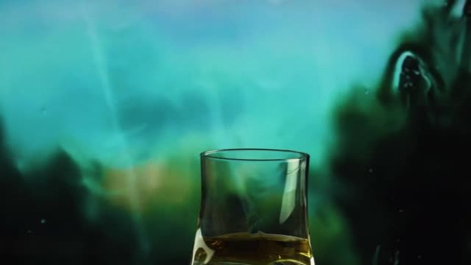 一杯威士忌在窗外雨中的背景下，威士忌在玻璃杯中特写。