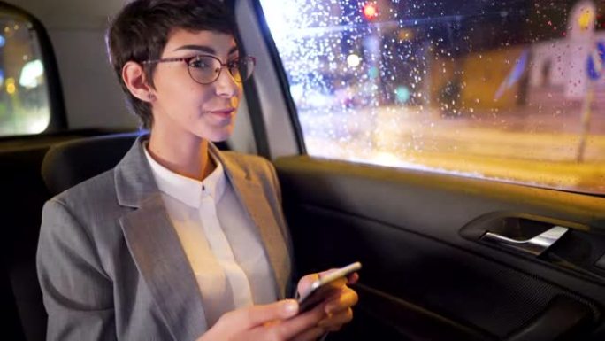 年轻的女商人在汽车后座上开车时使用智能手机