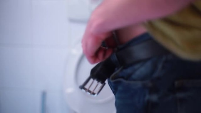 大便后，公共厕所里的一名男子用拉链拉紧裤子和皮带