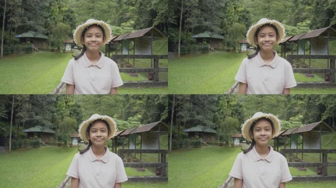 戴着草帽的肖像可爱女孩在森林公园停留时微笑着。女性青年志愿者向导站在草坪上迎接热带森林的游客。