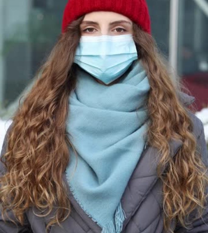 站在街上的白种人年轻卷发女性戴着医用口罩的纵向照片。大流行性流感电晕病毒。疫情冠状病毒。人群患病新型