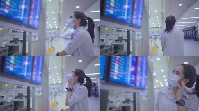 亚洲年轻女子戴着口罩看着机场航班时间表屏幕，女子迷路找不到登机柜台旅行行程预订，在机场航站楼，电晕病