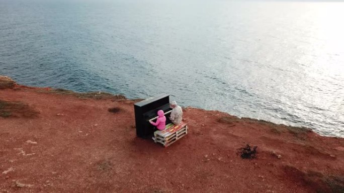 无人机的观点-女孩和老人在荒芜的海滨上一起用旧钢琴演奏
