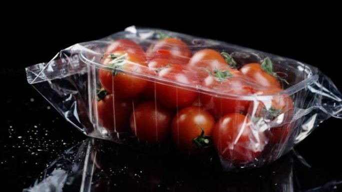 用油布包裹的塑料盒中的红色新鲜樱桃番茄在黑色背景上透明旋转