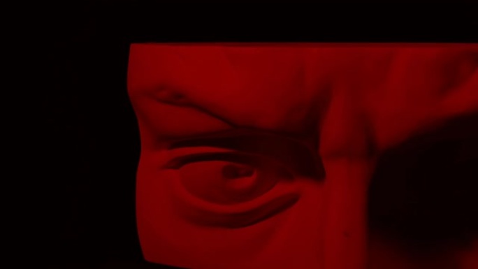 旋转石膏头的史诗工作室拍摄，带有移动和变化的红色照明。人类雕像一半脸上的光影游戏。在黑色背景上隔离4