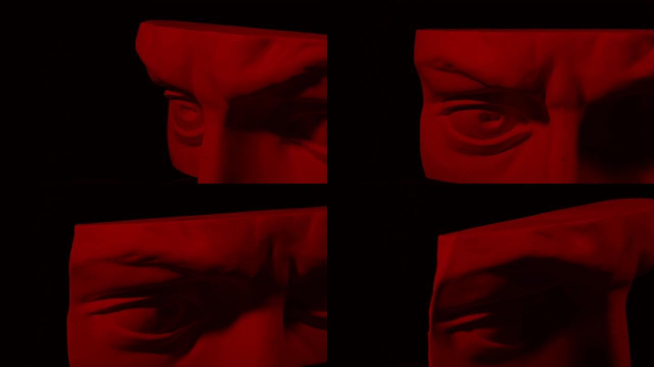 旋转石膏头的史诗工作室拍摄，带有移动和变化的红色照明。人类雕像一半脸上的光影游戏。在黑色背景上隔离4