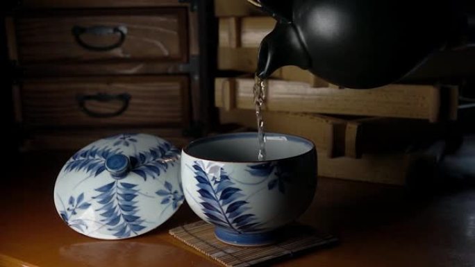 淡淡的日本茶从一个深棕色的陶罐倒入一个旧的碎裂的不温不火的白色瓷杯中