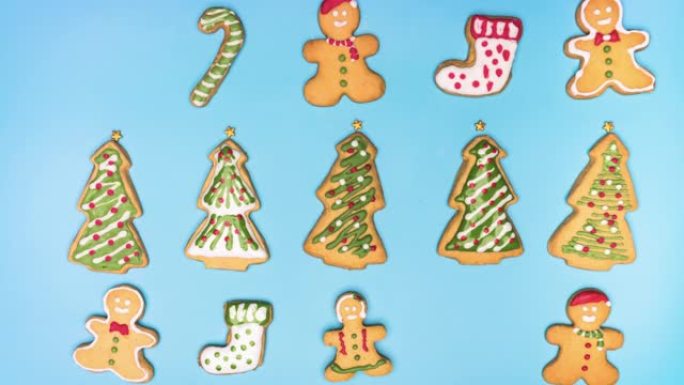停止运动平躺视图: 白色糖霜如雪落下，装饰糖霜，自制圣诞饼干，如姜饼，圣诞树，甘蔗和袜子在一张蓝色背