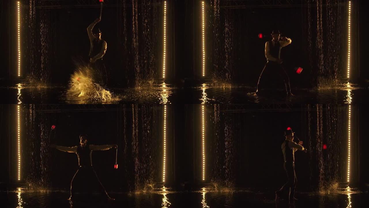 一位凉爽的火表演艺术家站在水面上时，用发光的LED手榴弹表演技巧。一个男人在雨中在黑暗的工作室里表演