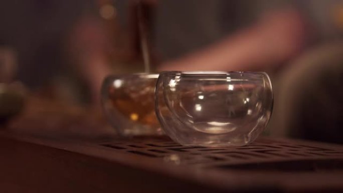 中国省份茶室的舒适氛围。瓷茶壶里的一股香茶充满了两个玻璃碗。特写，暖光。慢速