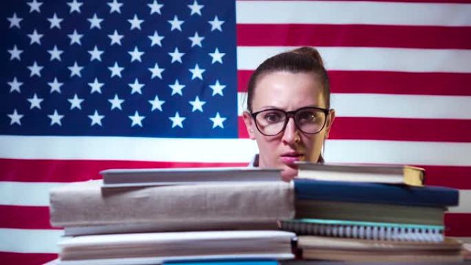 戴眼镜的学生女孩从书本下面窥视，对美国国旗背景上的书籍数量感到震惊。美国学生，美国学生。美国的教育