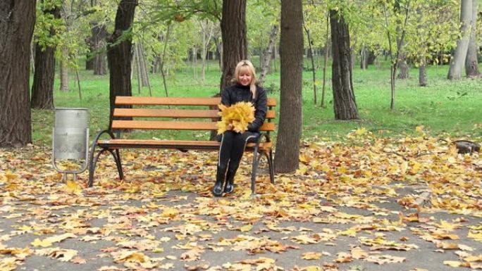金发女人坐在公园的长椅上。阳光明媚的秋天