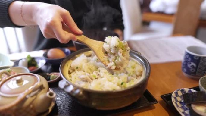 年轻女子在日本餐厅将米饭 (donabe gohan) 端到碗中