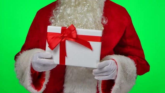 戴着白手套的胡须和红色西装的圣诞老人手里拿着礼品盒。被隔离在工作室的绿屏上。色度键。特写。慢动作