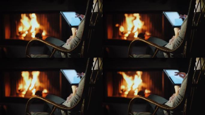 一名妇女坐在家里壁炉旁的摇椅上使用平板电脑