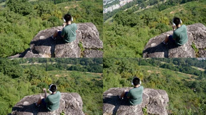 在阳光明媚的日子里，带着自然背景，模糊的亚洲男孩在山顶上戴着耳机听音乐。
