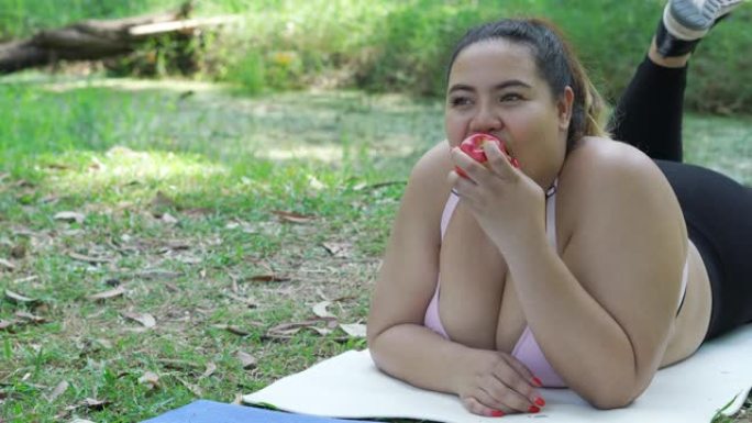 超重的女人在运动垫上吃苹果