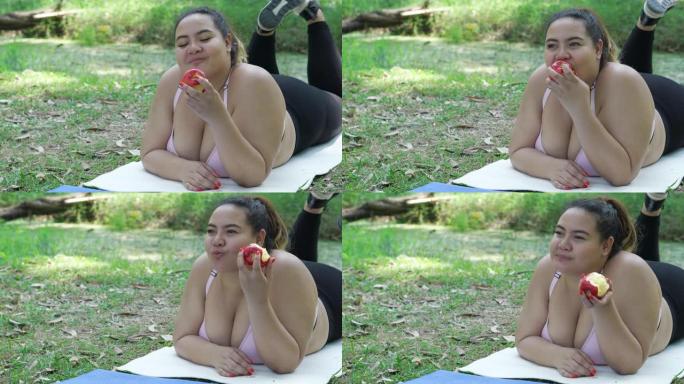 超重的女人在运动垫上吃苹果