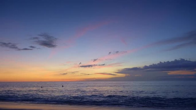 日落后，冲浪者在高潮的深蓝色海浪中游泳，海滩上有戏剧性的天空和紫色的云彩