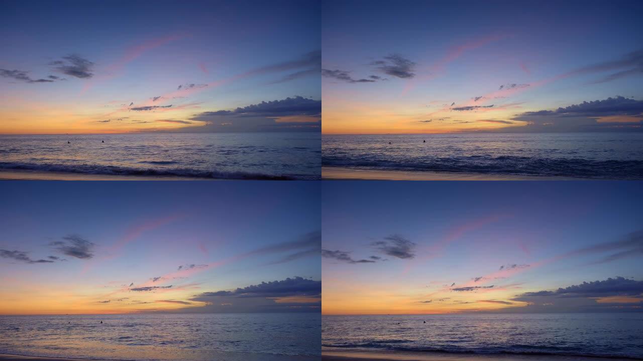日落后，冲浪者在高潮的深蓝色海浪中游泳，海滩上有戏剧性的天空和紫色的云彩