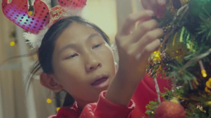 快乐的亚洲女孩穿着红色毛衣装饰圣诞树，晚上在家，节日概念。