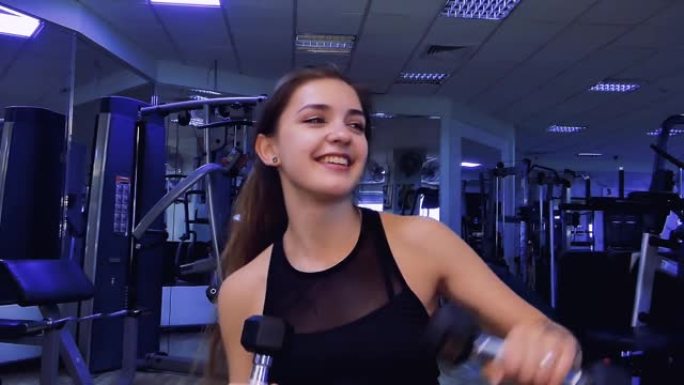 在两次锻炼之间，健身房里一位美丽的年轻女子手里拿着哑铃跳舞。