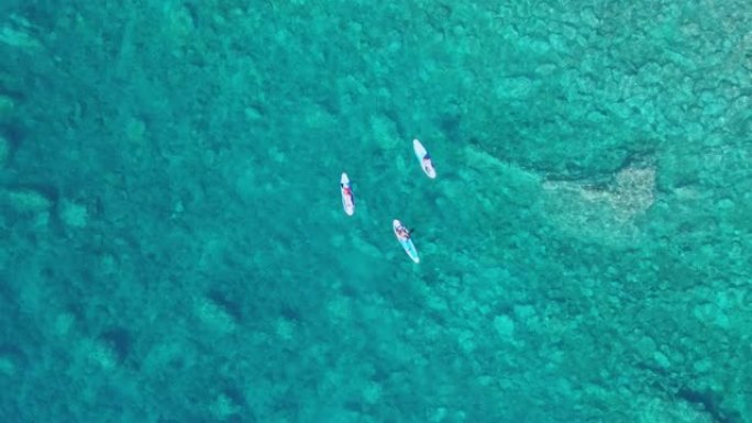 三个快乐的朋友在度假或度假时，在清澈的绿松石海中游泳、放松和享受日光浴。无人机在水面上方升起射击