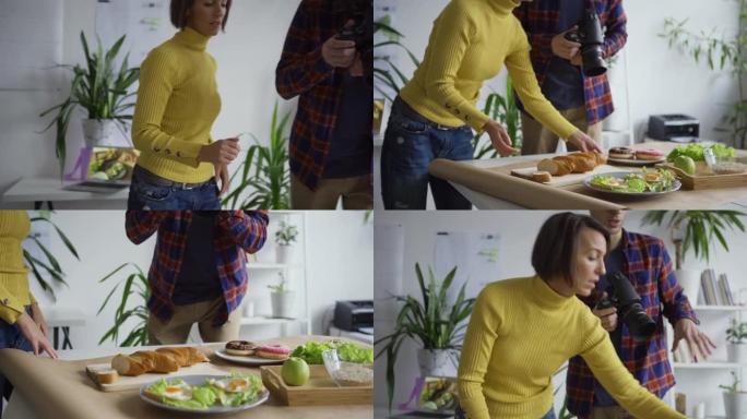 缩小女制片人在笔记本电脑上检查食物平的照片，并帮助年轻的男摄影师在工作室的桌子上布置物品