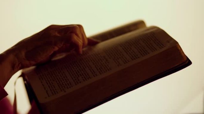 一个女人的手在明亮的灯光下剪影，手里拿着一本圣经，一边翻着几页。