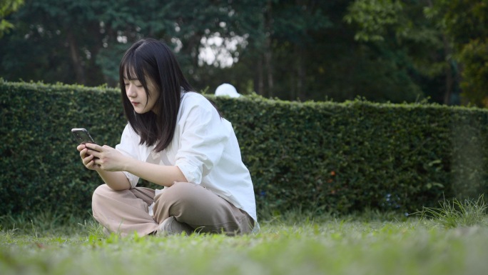 女孩坐在草地上玩手机