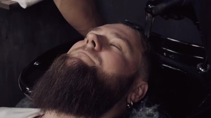 理发师在理发店里给一位大胡子顾客洗头。