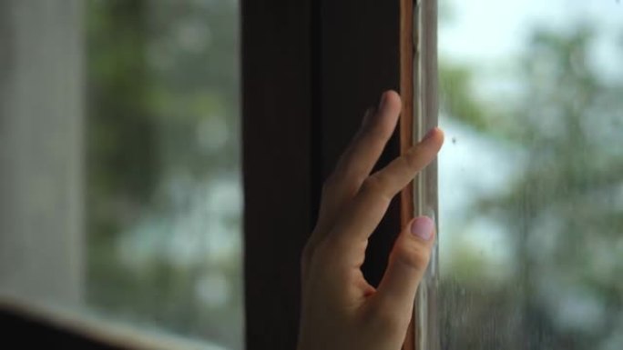 欧洲女孩站在窗户后面的房子里，用手触摸木框