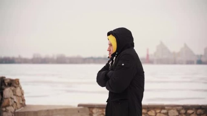 穿着黑色夹克的年轻冻人从寒冷中跳下来，站在街上。成年男性在冬季因寒冷而畏缩