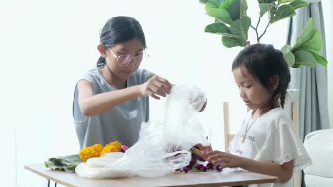 快乐的亚洲孩子在家里一起制作kathong (用香蕉叶和花朵制成，漂浮在河中祈祷和感谢)，为晚上做准