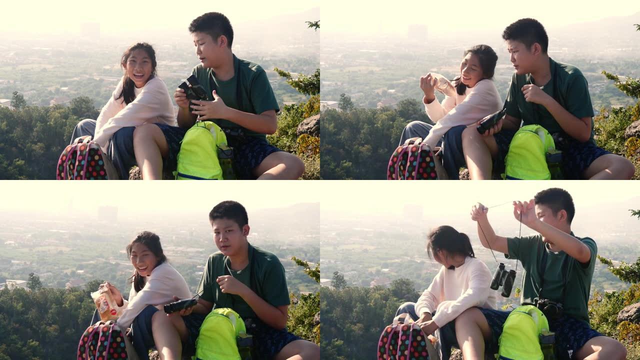 亚洲男孩和女孩坐在山顶上，看着风景，整理他们的背包。