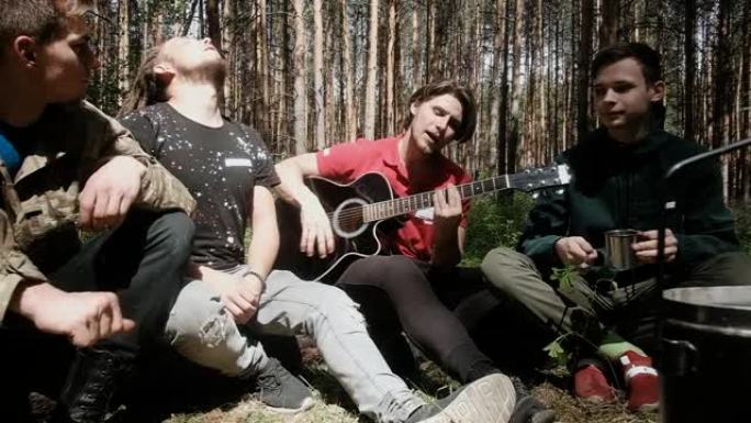 男人们坐在树林里的火炉旁。他们在徒步旅行时弹吉他。他们快乐地唱歌。有趣就是有趣。自然界中积极的生活方