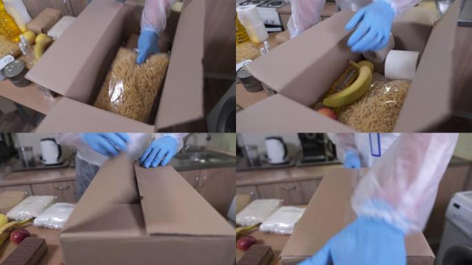 男性社会工作者志愿者将食物放在要发送的纸板箱中，穿着医疗服和口罩以保持卫生条件。人道主义和社会援助主