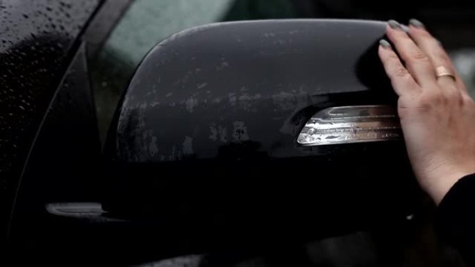 一名妇女从雨滴中擦拭汽车的后视镜。