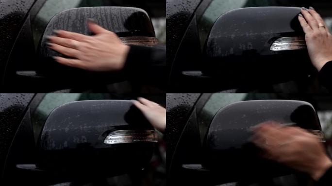 一名妇女从雨滴中擦拭汽车的后视镜。